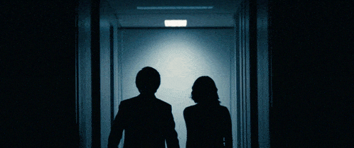 a man and a woman walking down a hallway holding hands