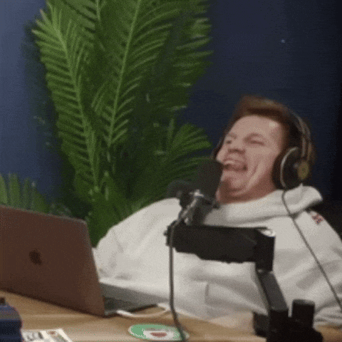 a man wearing headphones is laughing into a microphone while sitting in front of a laptop .