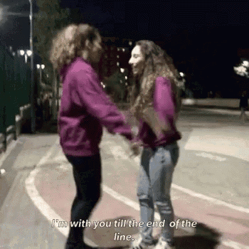 two girls are holding hands on a street at night and one of them says `` i 'm with you till the end of the line ''