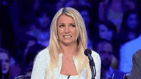 britney spears is sitting in front of a microphone making a funny face .
