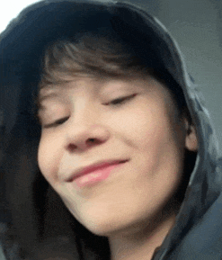a young boy wearing a hooded jacket is smiling with his eyes closed