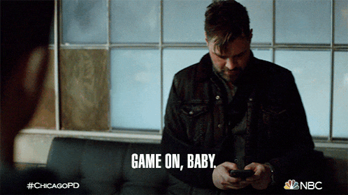 a man is sitting on a couch looking at his phone and the words game on baby are visible