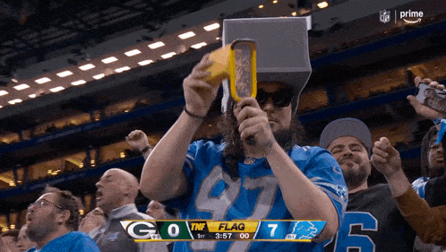 a man in a detroit lions jersey is holding a yellow object in front of a scoreboard