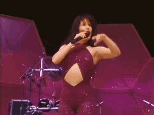 a woman in a purple jumpsuit is singing into a microphone on a stage .