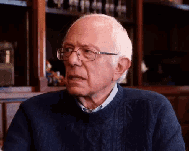 a man wearing glasses and a blue sweater looks to his left