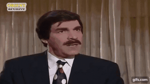 a man with a mustache wearing a suit and tie is making a funny face .