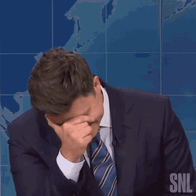a man wearing a suit and tie is smiling in front of a snl logo