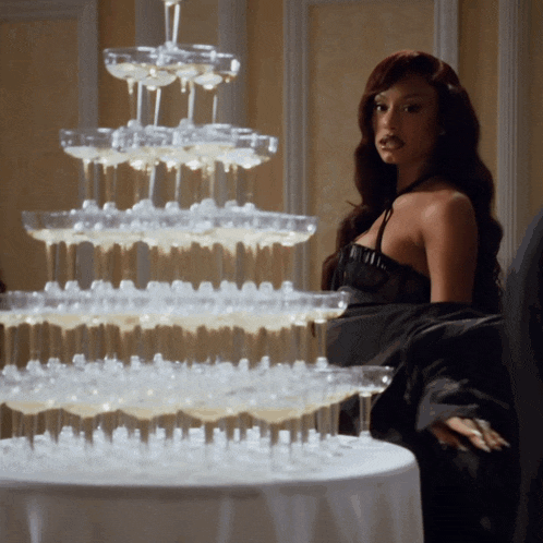 a woman in a black dress sits in front of a stack of champagne glasses
