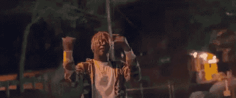 a man with dreadlocks is standing in front of a fence with his arms in the air .