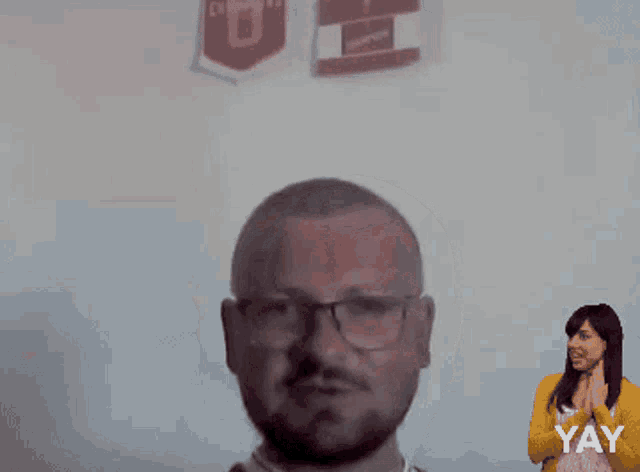 a man wearing glasses stands in front of a sign that says ' yay ' on it