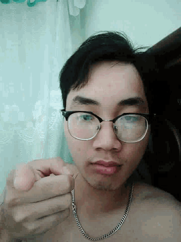 a man wearing glasses and a chain around his neck is laying down
