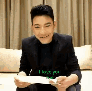 a man in a suit is sitting on a couch holding a piece of paper that says `` i love you '' .