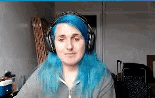 a woman with blue hair wearing headphones looks at the camera