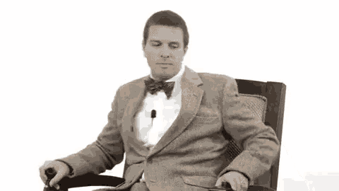 a man in a suit and bow tie is sitting in a chair with a cane in his hand .