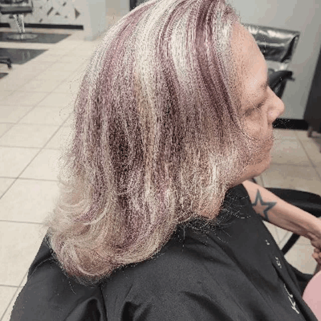 a woman with gray and purple hair is sitting in a chair in a hair salon .