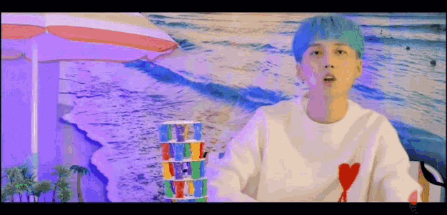 a boy with blue hair is holding a stack of cups in front of a beach .