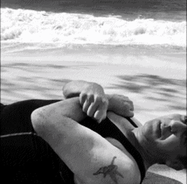 a woman with a tattoo of a starfish on her arm is laying on the beach