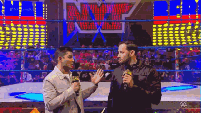two men are talking to each other in front of a wrestling ring