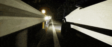 a white car is driving down a highway at night with the headlights on .