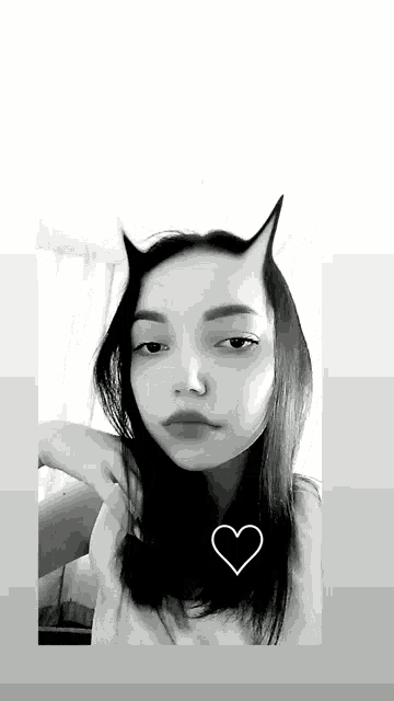 a black and white photo of a woman wearing devil horns and a heart .