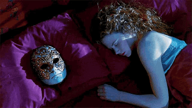 a woman is sleeping in a bed next to a mask