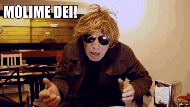 a man wearing sunglasses and a brown jacket says " molime dei "