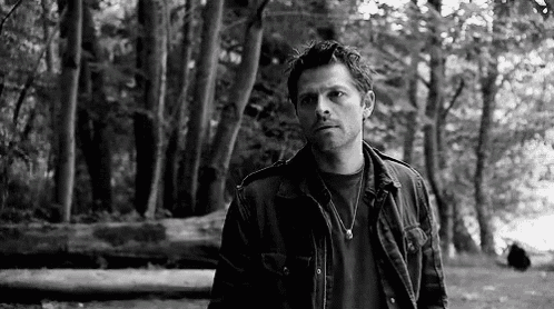 a man in a jacket and necklace is standing in a forest .