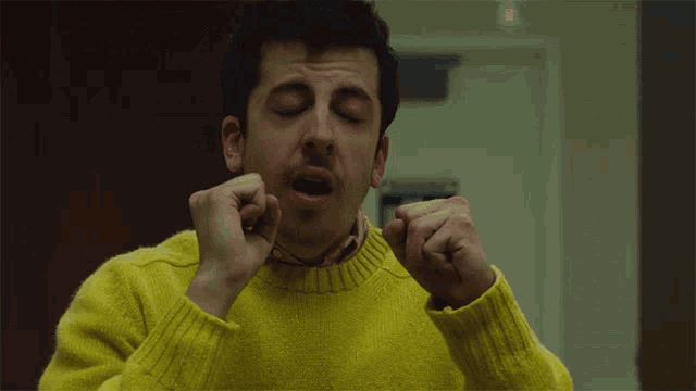a man wearing a yellow sweater covering his mouth with his hands