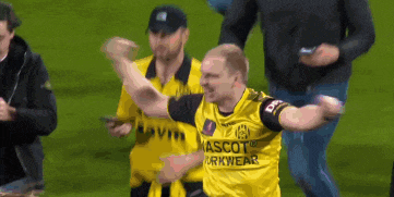 a man in a yellow mascot workwear shirt celebrates on a field