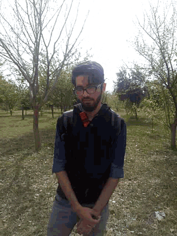 a man wearing glasses and a backpack stands in the grass