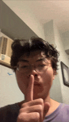 a man wearing glasses holds his finger to his lips