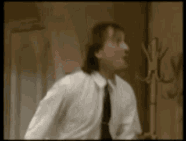 a man in a white shirt and tie is standing in a room with a coat rack in the background .