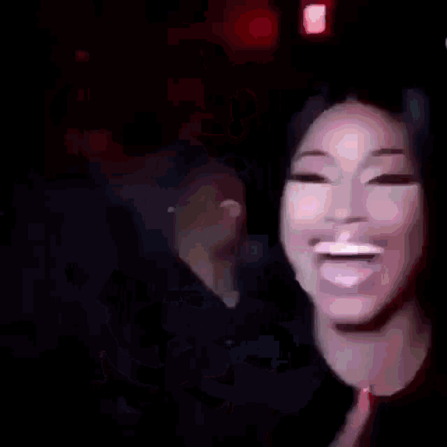 a close up of a woman laughing and giving a thumbs up in a dark room .