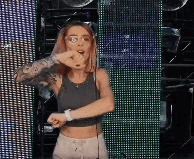 a woman wearing headphones and a crop top is dancing in front of a large screen .