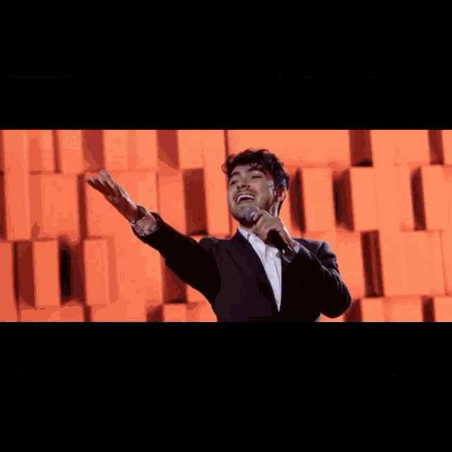 a man singing into a microphone while wearing a colorful jacket and jeans