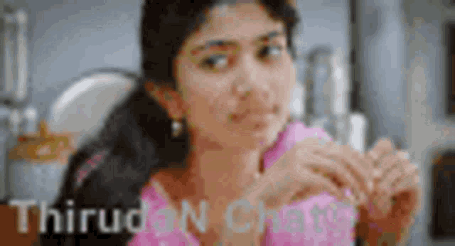 a woman in a pink dress is sitting in a kitchen with her hands folded .