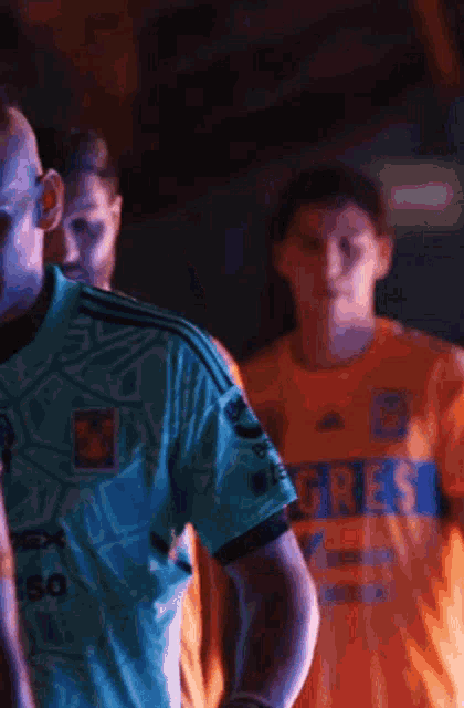 a man wearing an orange tigres jersey stands next to another man