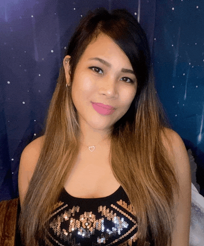 a woman wearing a black top with sequins and a heart necklace smiles for the camera