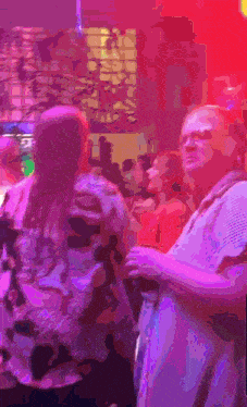 a group of people are dancing in a club with purple lights behind them