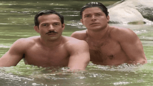 two men without shirts are swimming in a river
