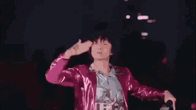 a man in a pink jacket is holding a microphone and singing into it .