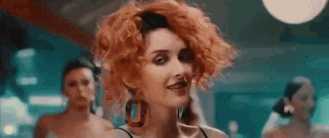 a woman with red curly hair is wearing a black top and earrings .