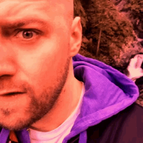 a close up of a man 's face with a purple hoodie on