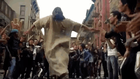 a man dressed as jesus is dancing in front of a crowd of people on a city street .