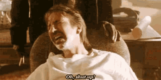 a man is sitting in a chair with shaving cream on his face and says `` oh , shut up ! ''