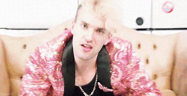 a man is sitting on a couch wearing a pink jacket and a chain .