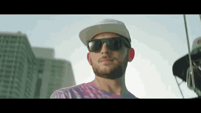 a man wearing sunglasses and a hat stands in front of a building