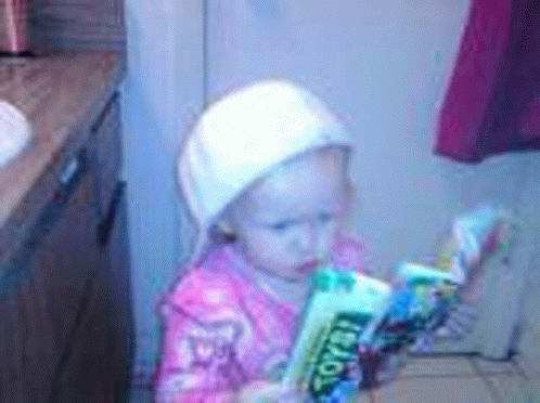 a little girl wearing a white hat is reading a book in a kitchen