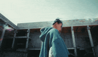 a woman wearing a blue hoodie stands in front of a concrete building