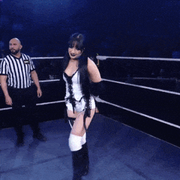 a woman in a corset is walking in a ring with a referee